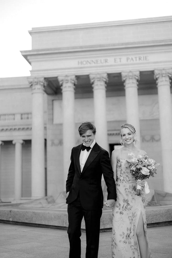 Jordan in a tuxedo and Maria in a floral gown walking hand in hand in front of the Legion of Honor in San Francisco.